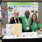 Two women and one man stand in front of colorful poster in conference center