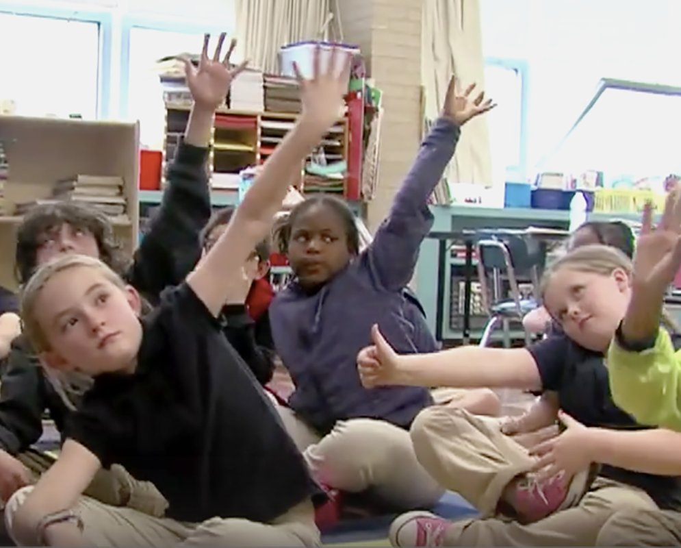 3rd graders on floor with raised hands