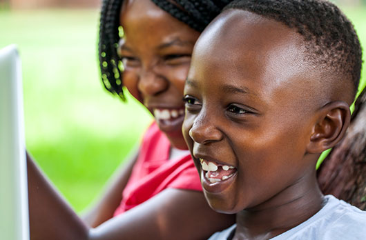 Two young children react with smiles to an unseen object.