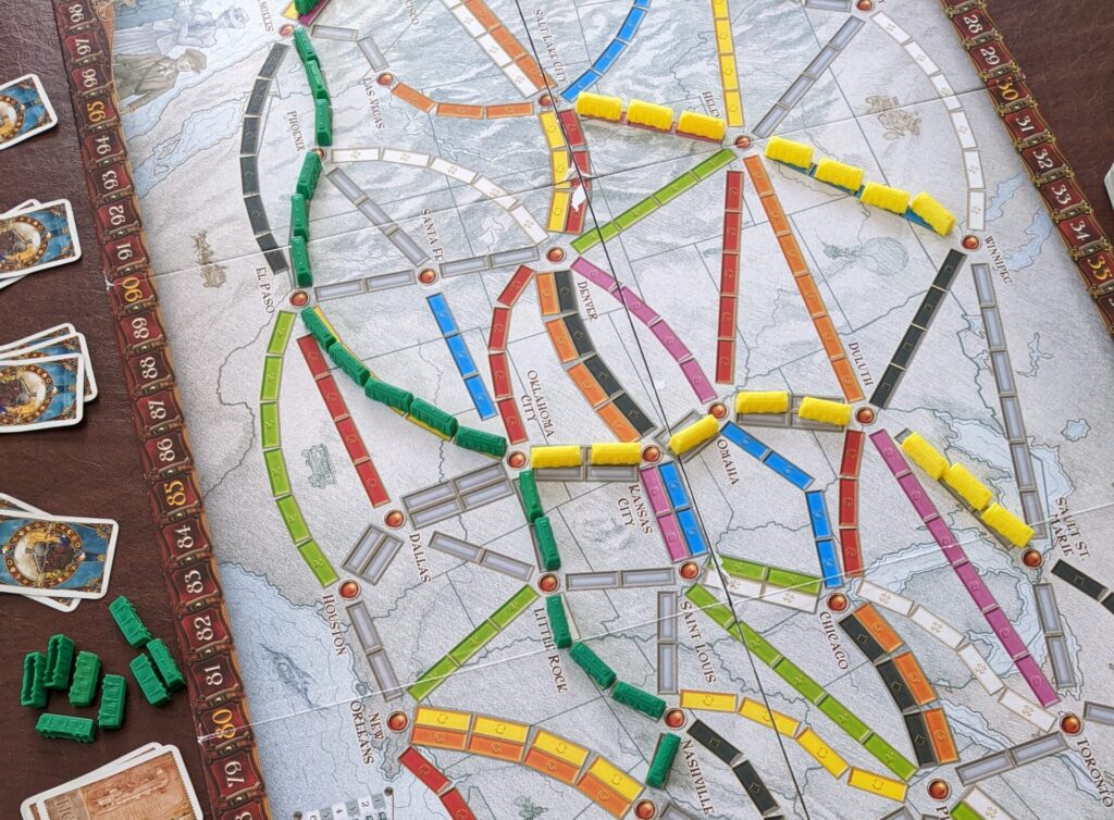 Ticket to Ride board game is set up on a. table with cards and pieces next to it. 