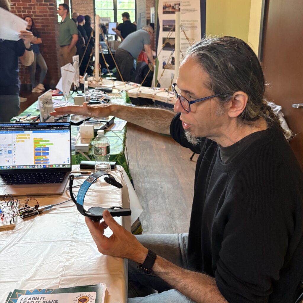 Adult demonstrates BCI headset in front of open laptop.
