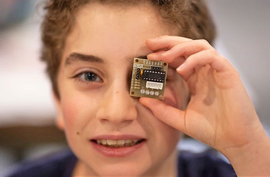 Close-up of a student holding a small circuit board up to one eye while participating in a NeuroVivid Pathways hands-on technology activity.